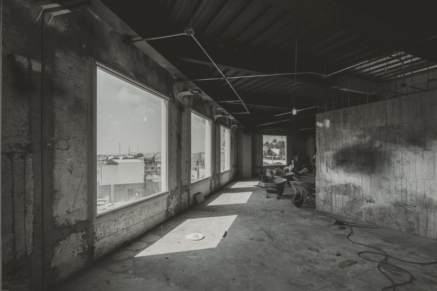 Building interior under construction, with an exposed ceiling, bare concrete walls and sunlight falling through tall windows