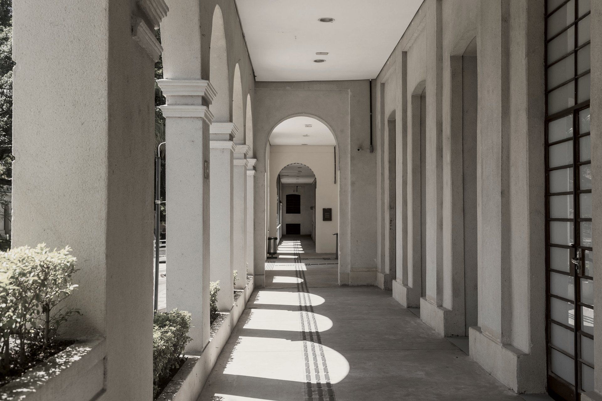 Sunlit arcade with arched openings and arch-shaped patches of light across the floor