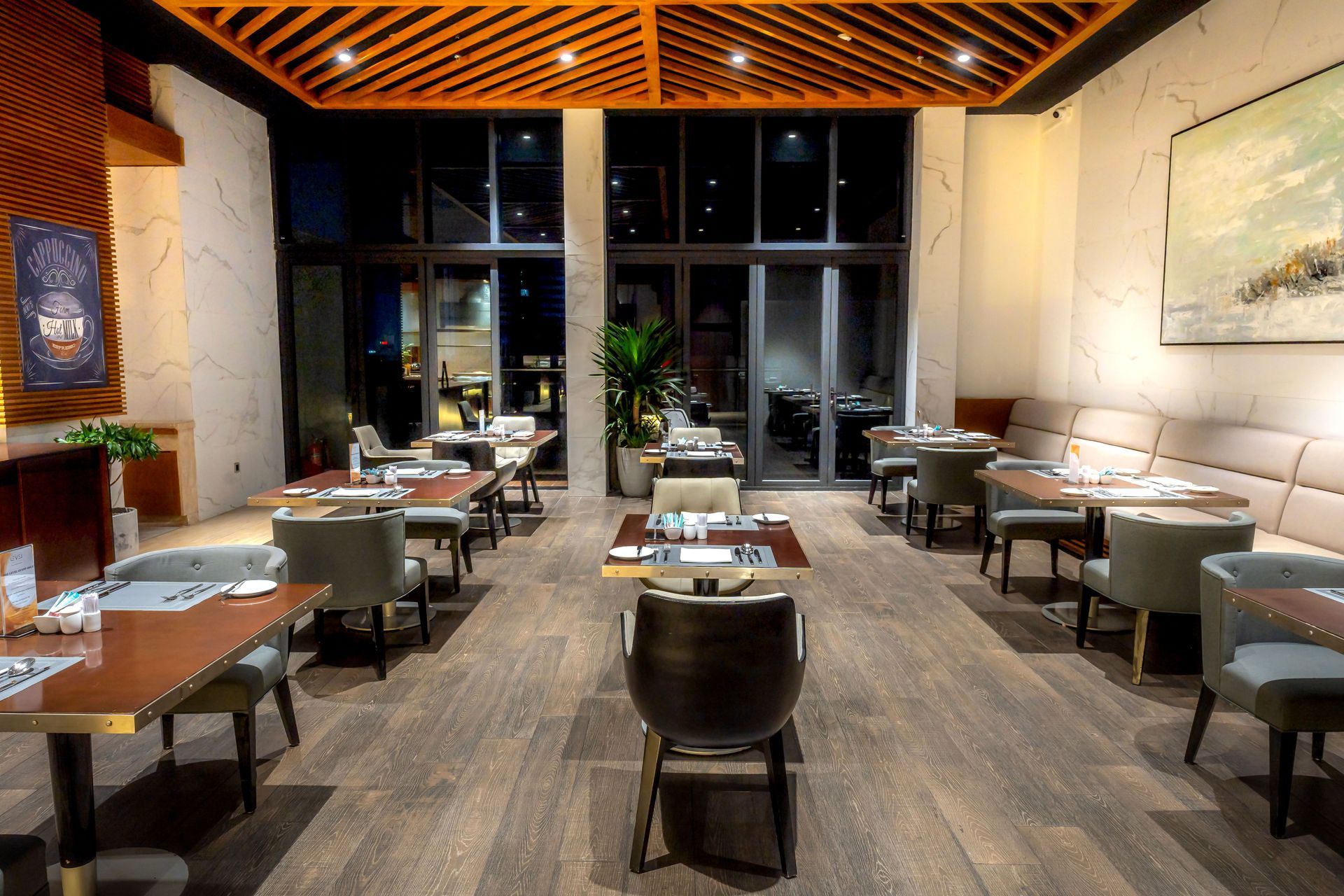 Modern restaurant dining room with neatly set tables, gray chairs, and large windows at the back