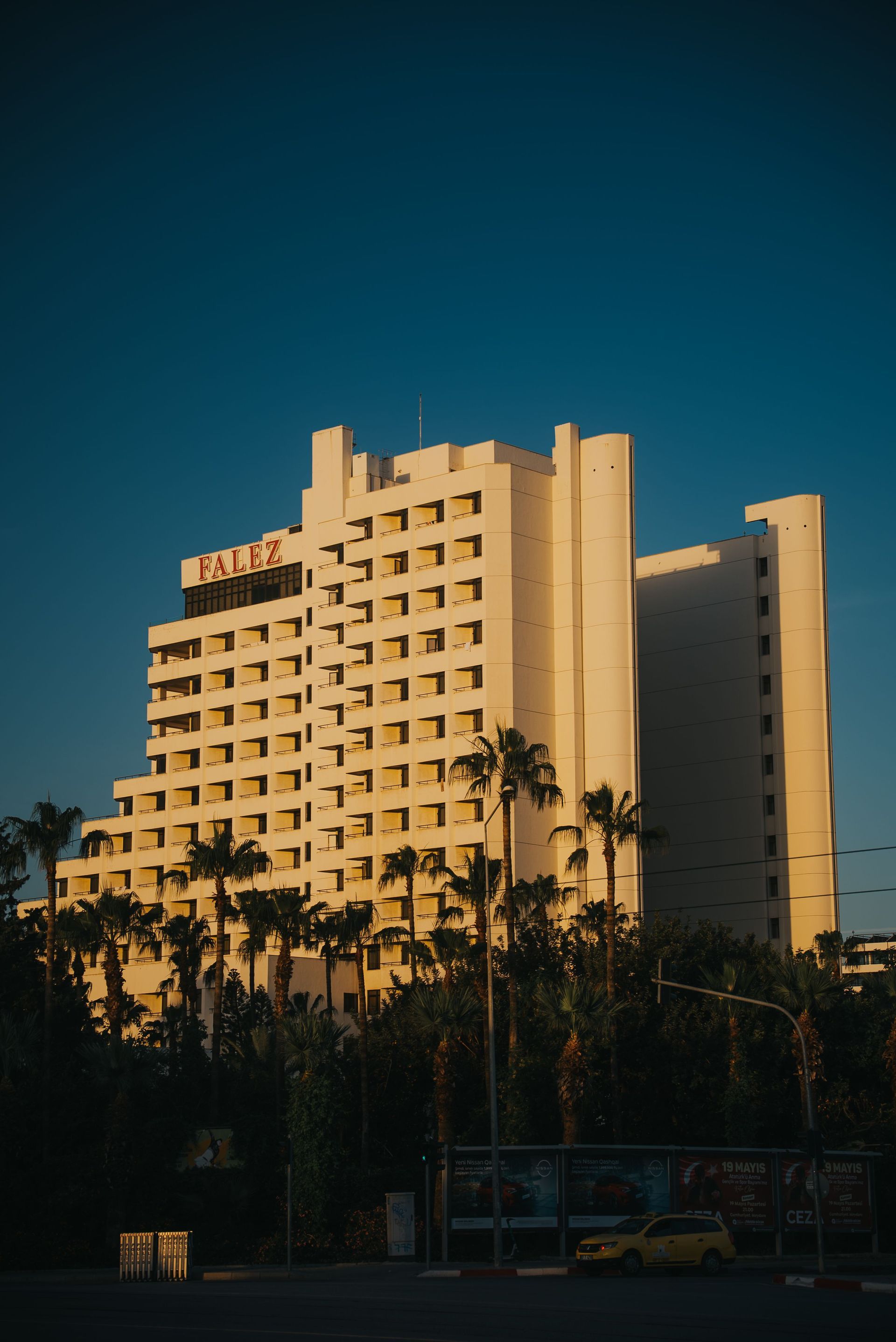 Sunlit beige hotel tower with palm trees against a deep blue sky at dusk