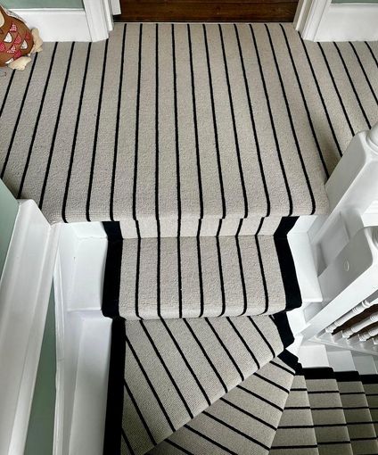 Staircase with cream carpet, black stripes, and white risers.
