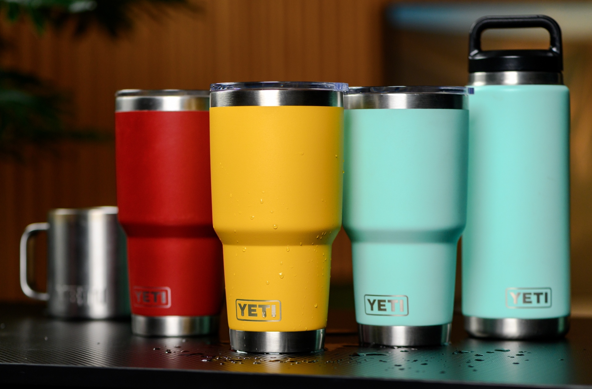 A row of yeti tumblers of different colors are sitting on a table.