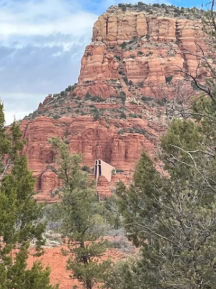A church on top of a red rocky mountain surrounded by trees.
