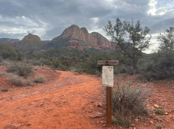 A wooden sign in the middle of a dirt road with mountains in the background.