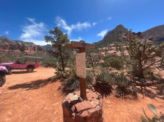 A pink jeep is parked next to a wooden sign in the desert.