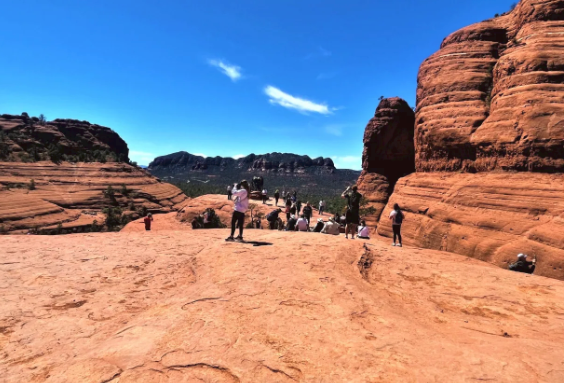 A group of people are standing on top of a sandy hill in the desert.