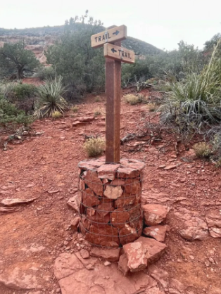 A wooden sign with two arrows pointing in opposite directions is sitting on top of a pile of rocks.