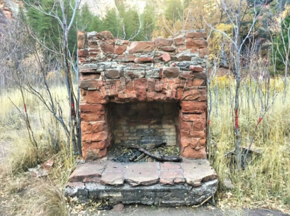 A brick fireplace in the middle of a field with trees in the background.