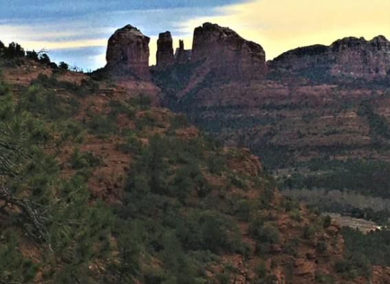 A mountain covered in trees and rocks with a sunset in the background.