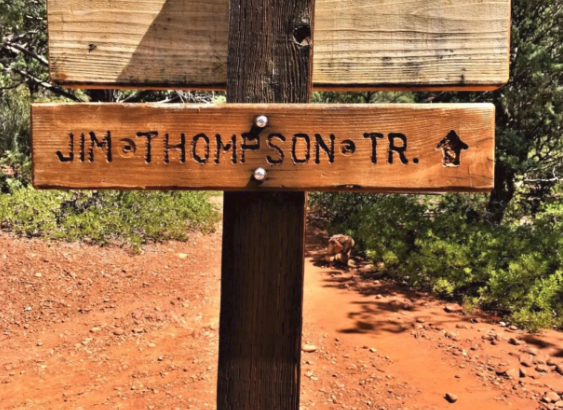 A wooden sign on a post shows the way to jim thompson trail.