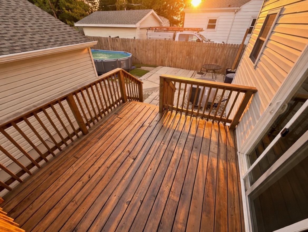 A high-angle view of a newly stained wooden deck with railings, overlooking a backyard with a pool at sunset.