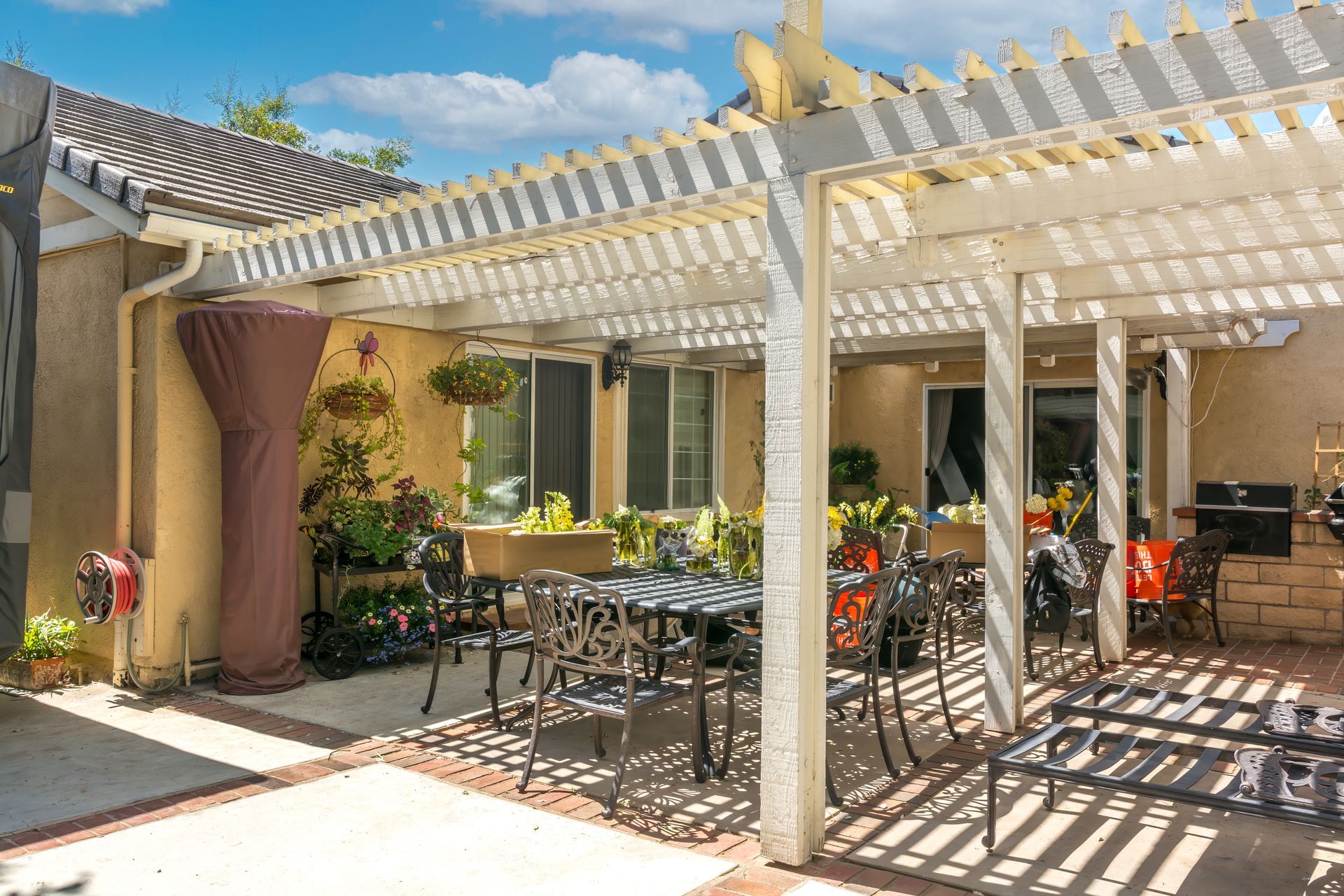 A patio with a white lattice pergola, metal outdoor dining furniture, potted plants, and a heater cover.