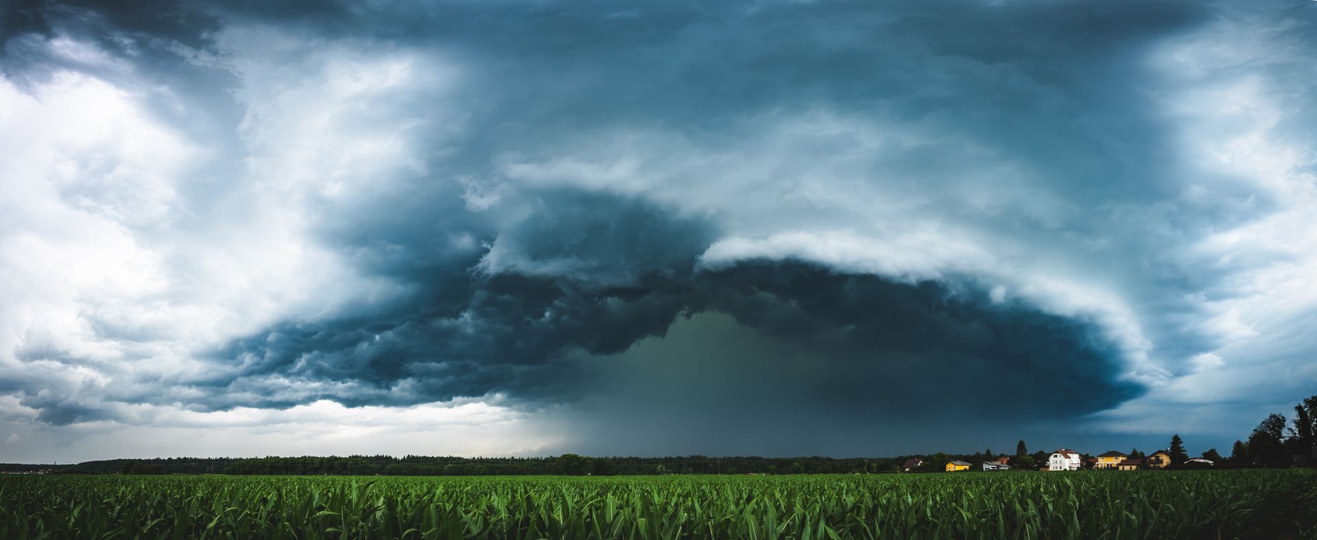 A dark, dramatic storm cloud hangs over a vast green field, with heavy rain falling in the distance.