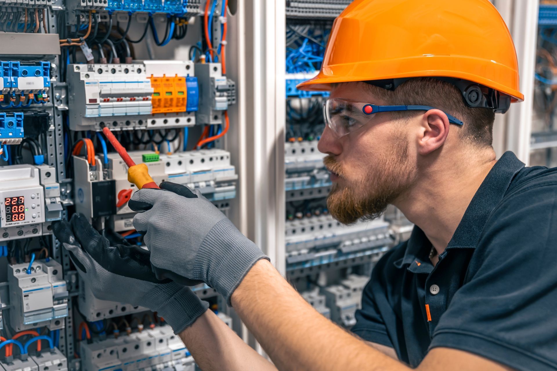 Electrician in orange hard hat adjusting wiring inside an industrial electrical control panel