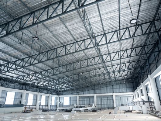 Empty industrial warehouse interior with high steel trusses and large windows, under construction