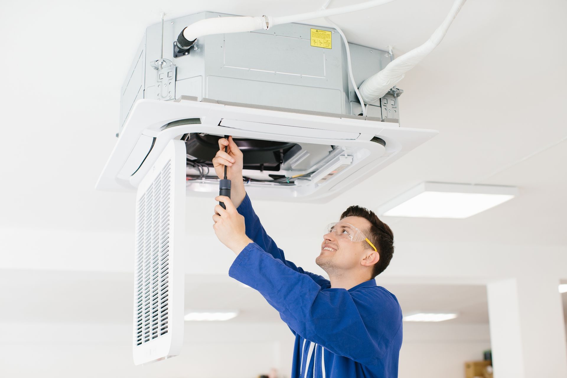 Technician adjusting a ceiling-mounted air conditioner in a bright office ceiling