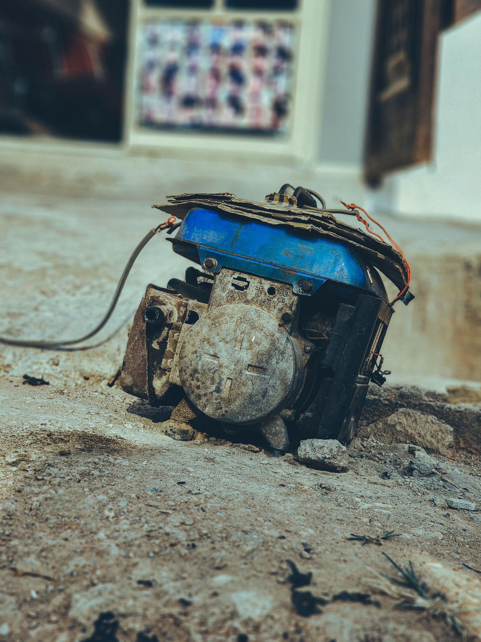Small blue and black robot lying on a dusty floor indoors, with wires exposed