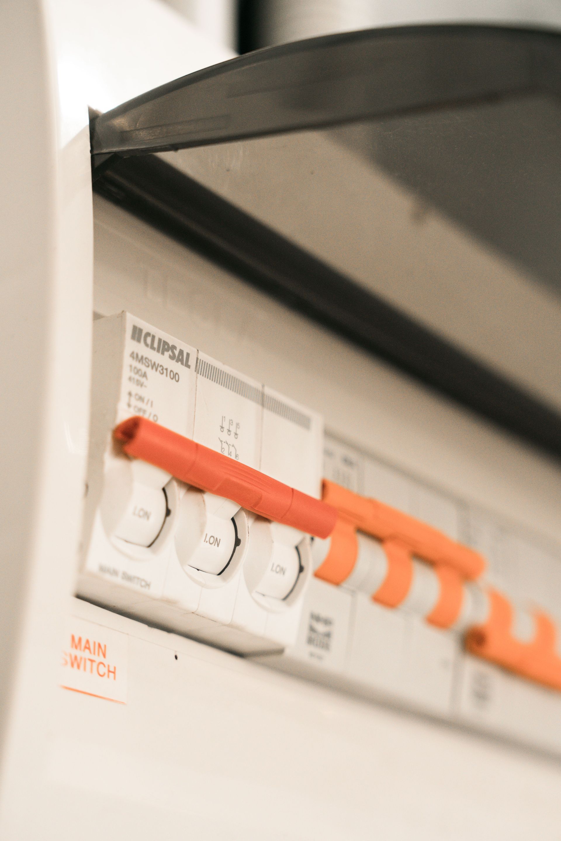 Close-up of a white electrical breaker panel with orange switches under a black cover.