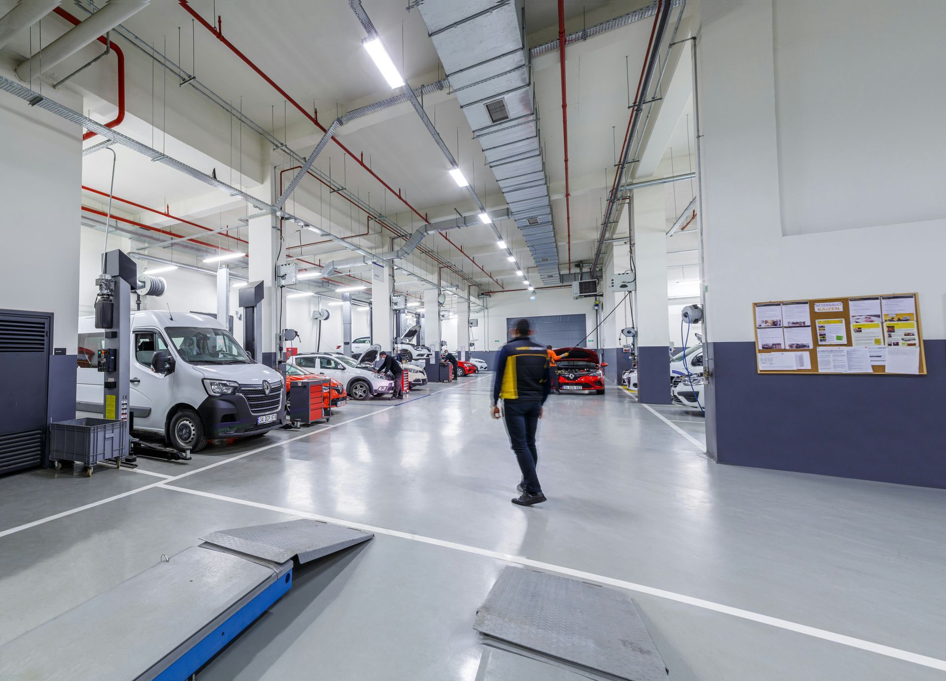 Person walking through a bright auto repair garage with cars and equipment along the walls