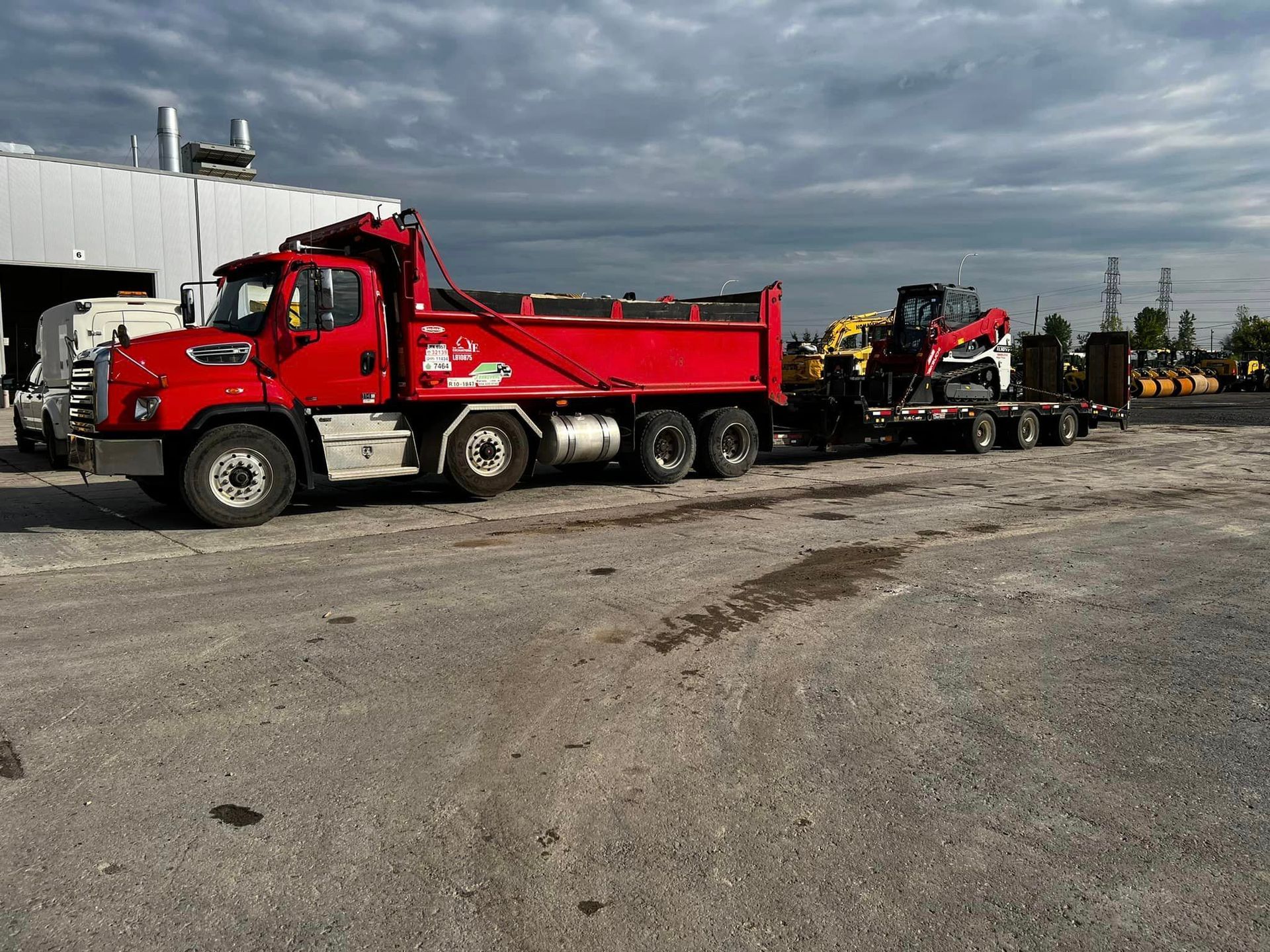 Un camion-benne rouge est garé sur un parking à côté d'un bâtiment.