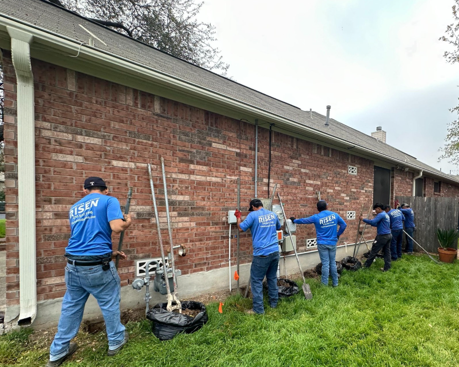 A crew of workers in blue shirts are installing electrical lines on a brick house wall.