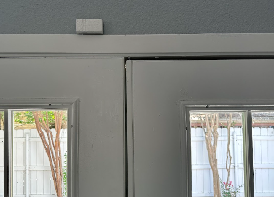 White double doors with glass panels; security sensor on the header. View outside through windows.