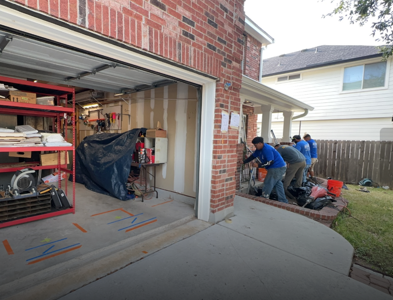 Four people working outside a house, likely on a yard project. Garage door open, tools visible. Four people working outside a house, likely on a yard project. Garage door open, tools visible.