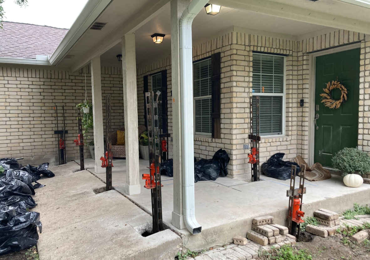 House porch with supports. Jacks prop up the roof, trash bags sit on the ground, and a green door. House porch with supports. Jacks prop up the roof, trash bags sit on the ground, and a green door.