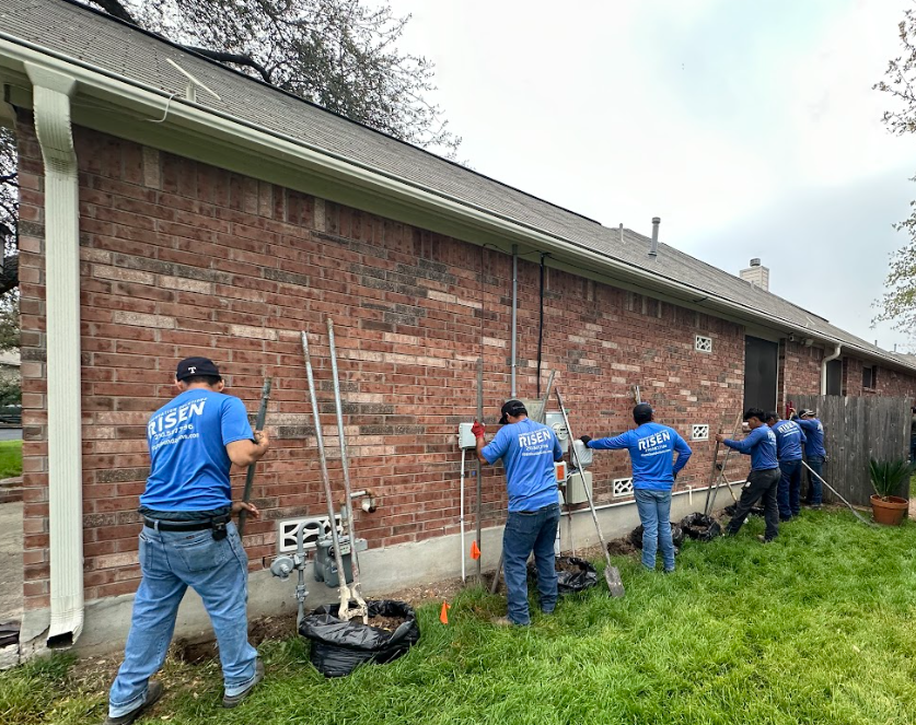Group of workers in blue shirts installing equipment on a brick building exterior.