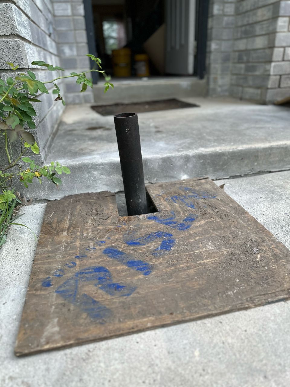 A metal pole is sitting on top of a wooden base on the sidewalk.