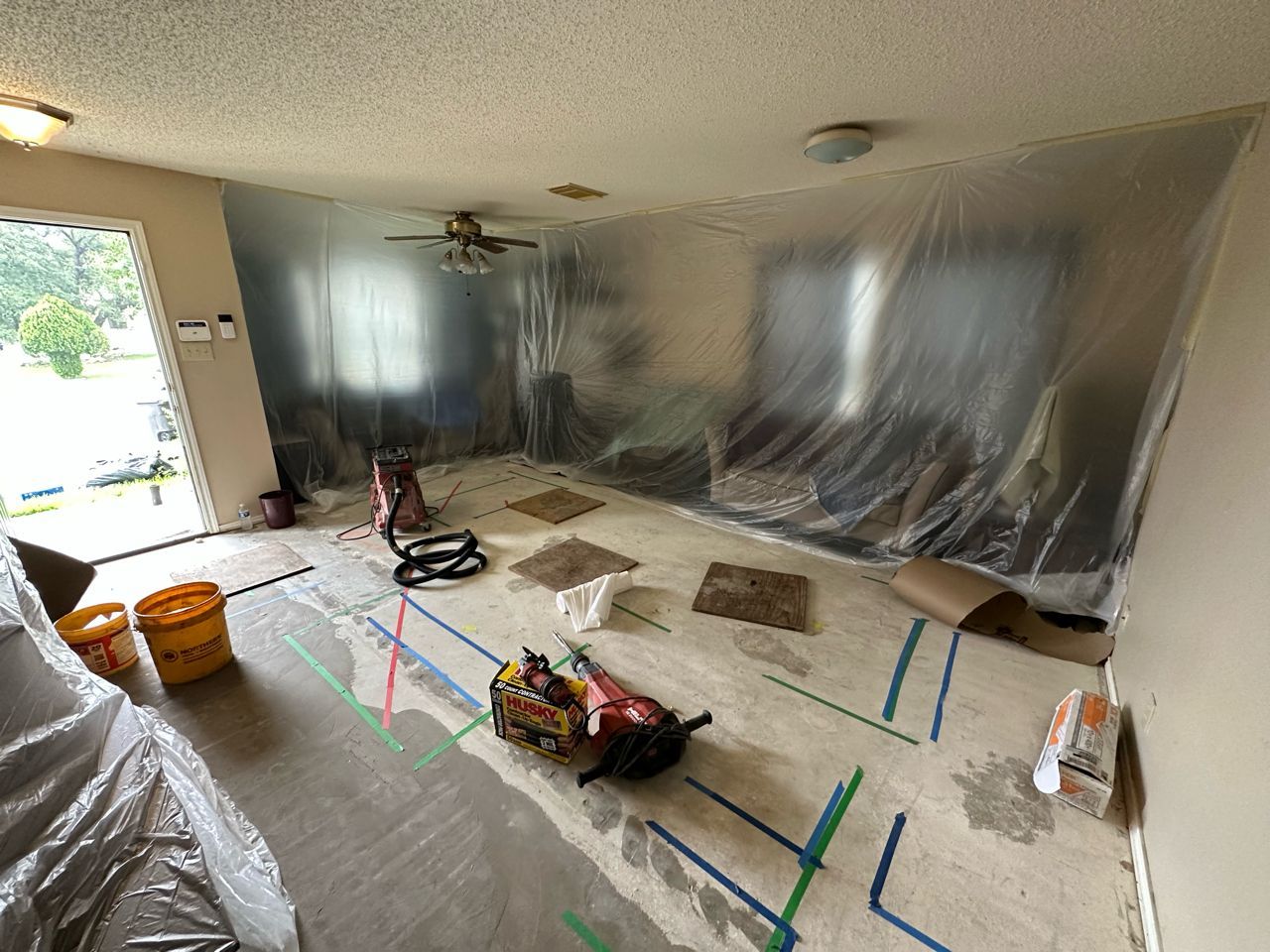 A living room is covered in plastic and tape.