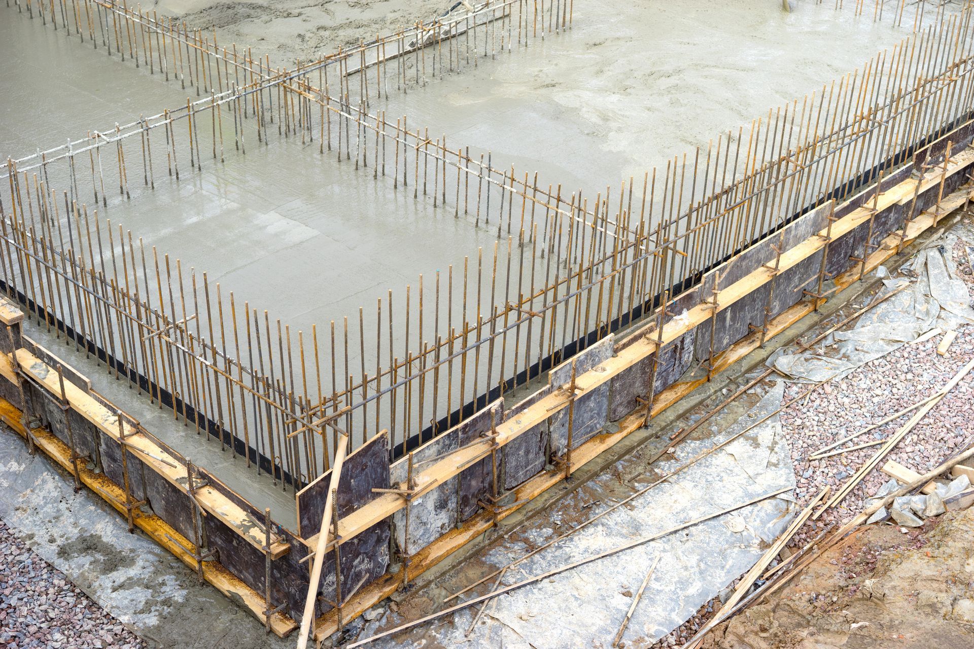 Concrete foundation slab with exposed rebar and wooden formwork at a construction site