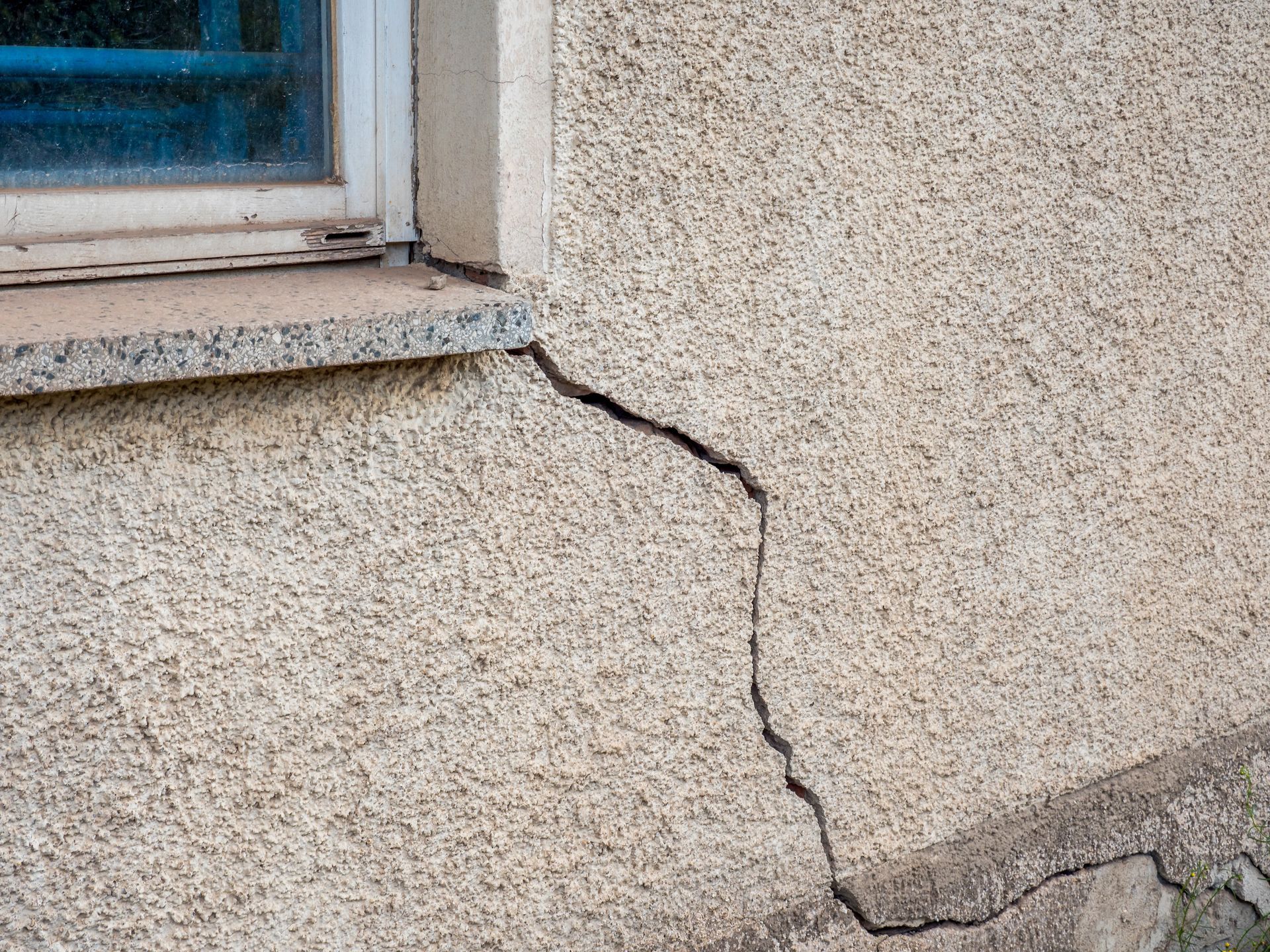 Exterior wall with large vertical crack near window and foundation. Exterior wall with large vertical crack near window and foundation.