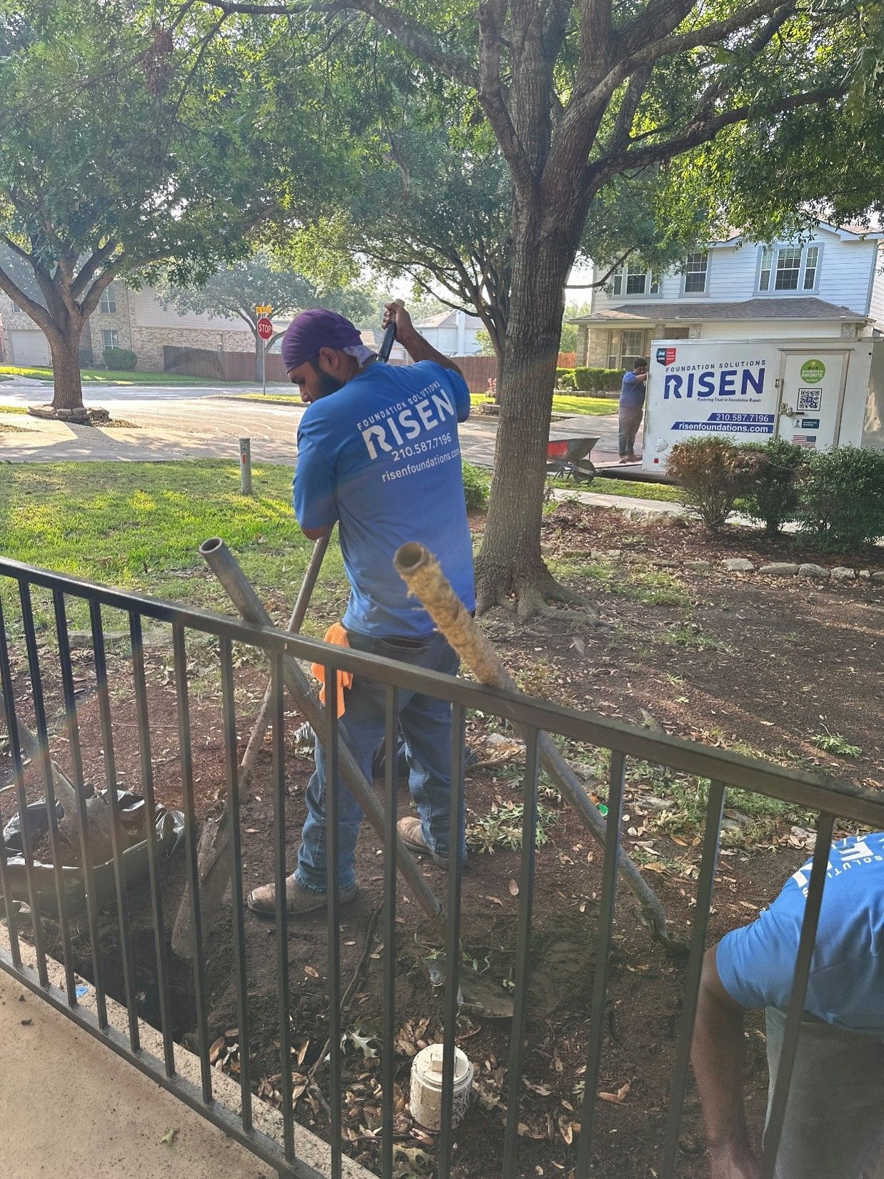 A worker from Risen Foundation Solutions is digging in a yard near a fence A worker from Risen Foundation Solutions is digging in a yard near a fence