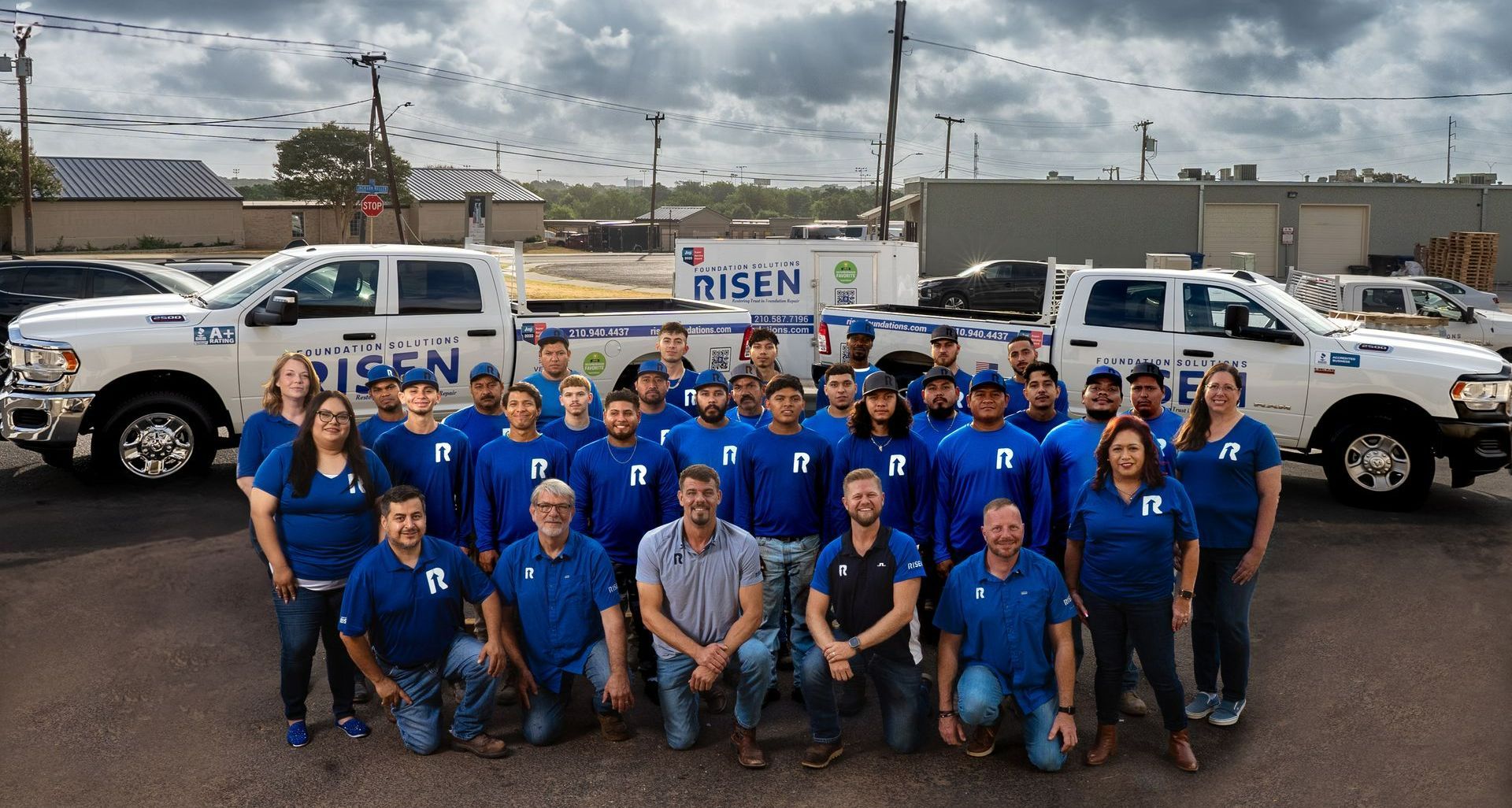 A large group of people are posing for a picture in front of trucks.