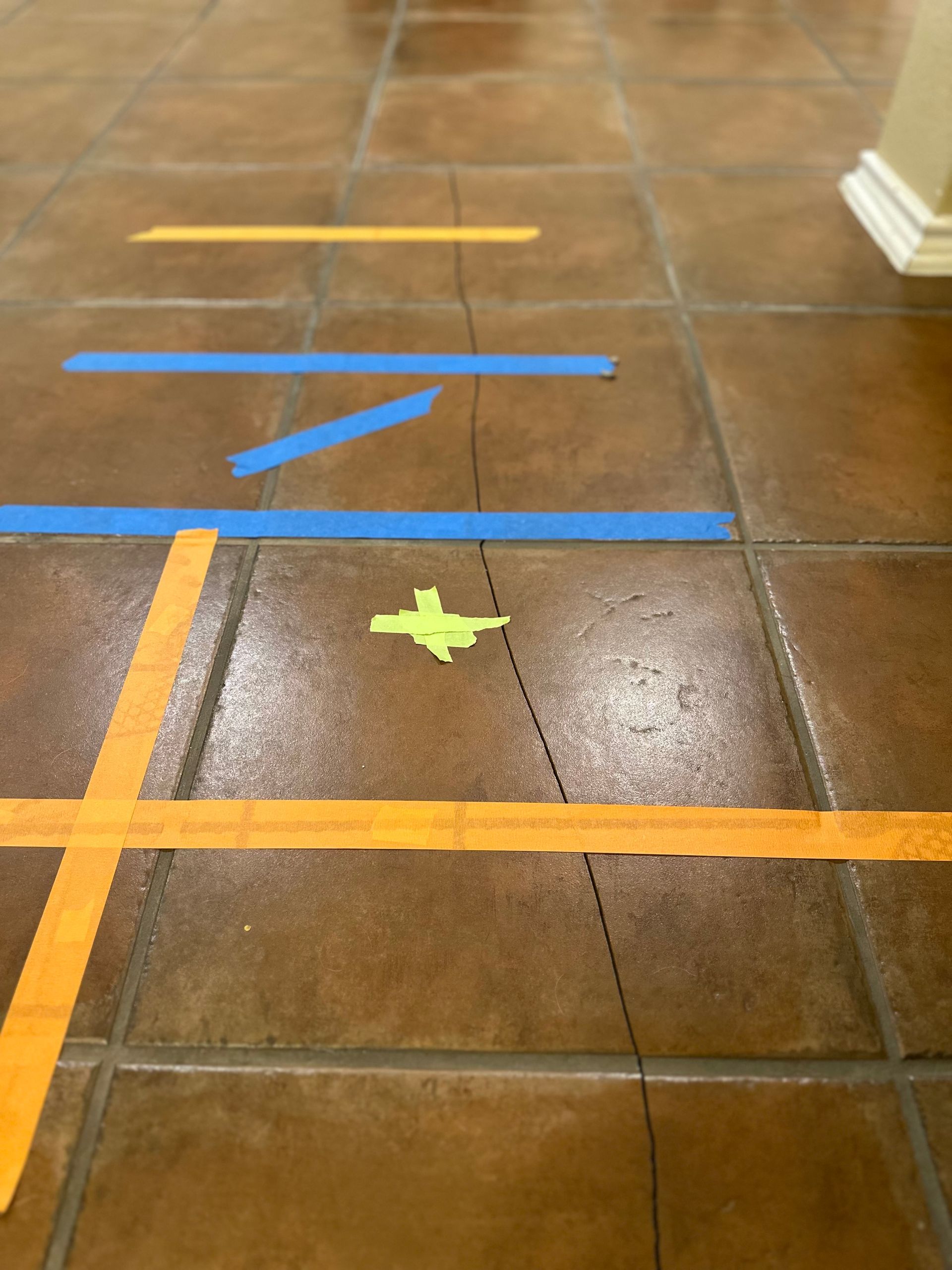 Brown tile floor with blue and orange tape, and a paper cutout in the center. A crack goes through the middle.