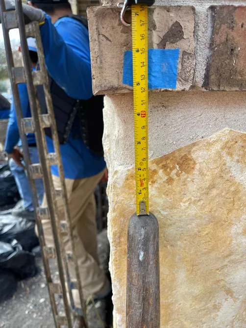 A man is measuring a brick wall with a tape measure.