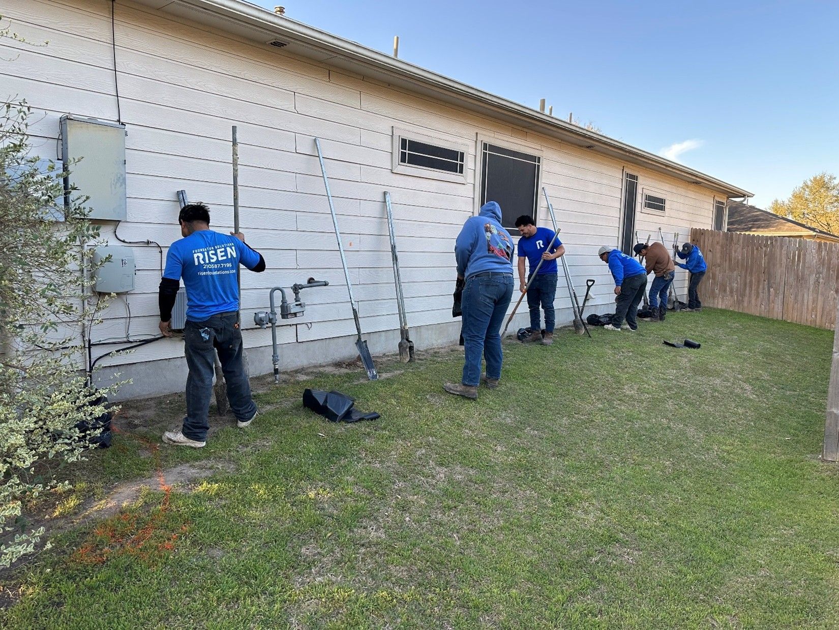 A group of people working on a house's exterior. They are on the lawn near a fence.