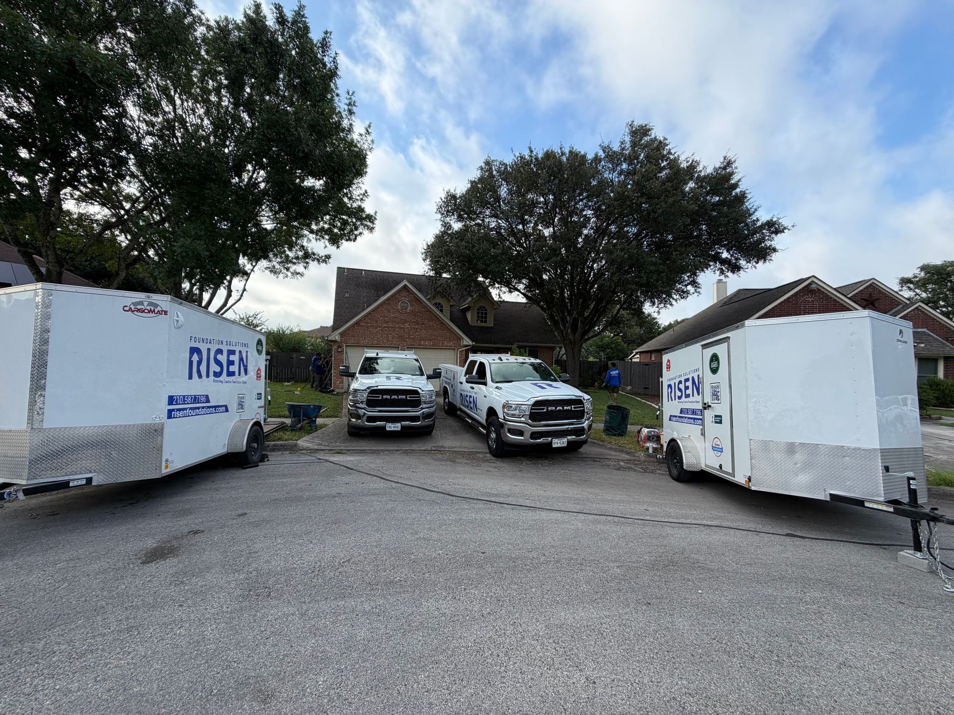 Two white moving trucks parked at a house driveway with two cars between them