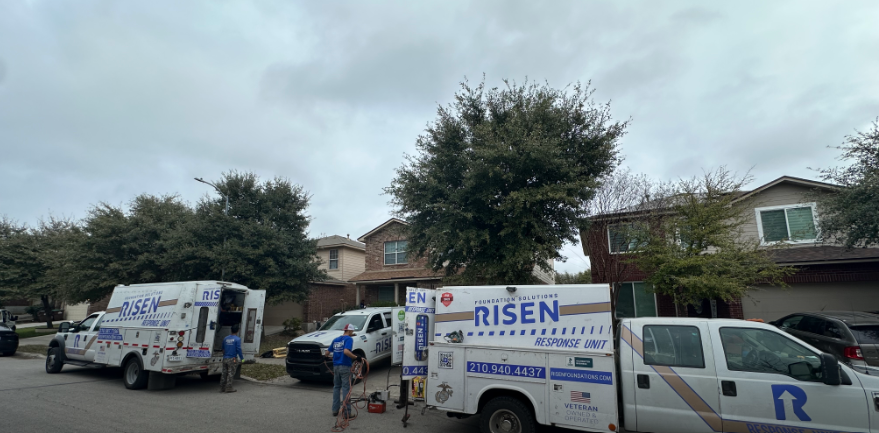 Service trucks parked in front of a two-story home, cloudy day. Risen company logos visible on the trucks. People working outside.