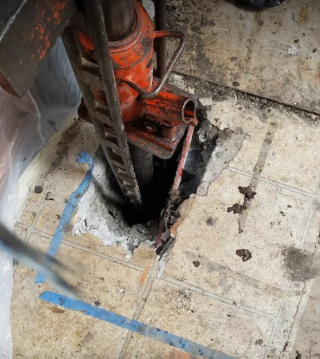 A hydraulic jack is sitting in a hole in the floor. Repairing foundation