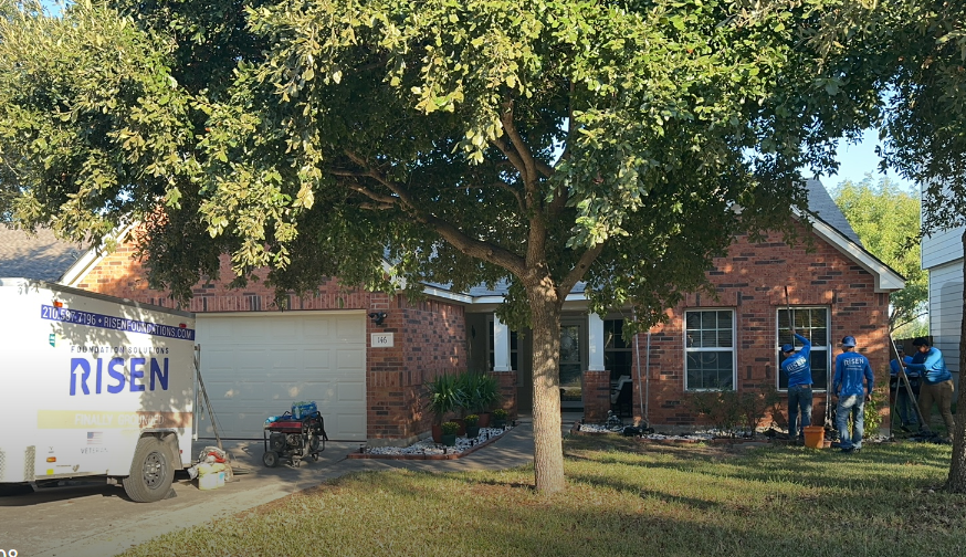 A white truck with the word risen on it is parked in front of a brick house