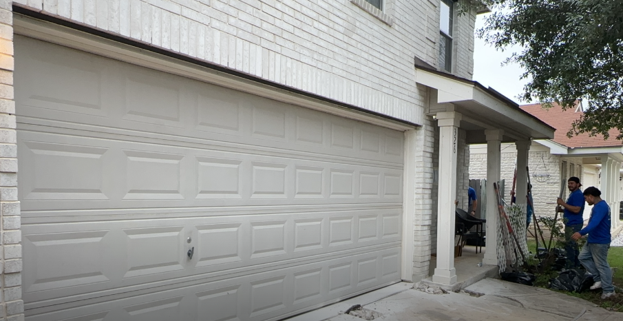 A group of men are standing in front of a white garage door. A group of men are standing in front of a white garage door.