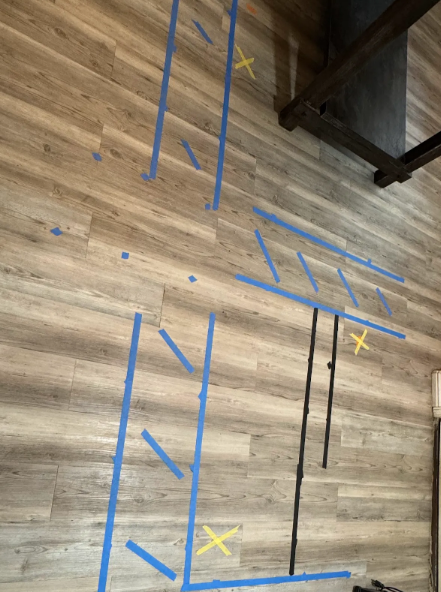 Blue tape outlines furniture placement on wood-look floor, with yellow 