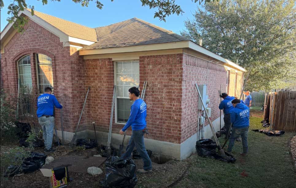 Construction workers in blue shirts are landscaping around a brick house. Construction workers in blue shirts are landscaping around a brick house.