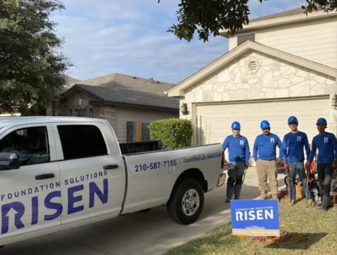 A group of men standing beside white truck A white truck with the word risen on it is parked in front of a house.