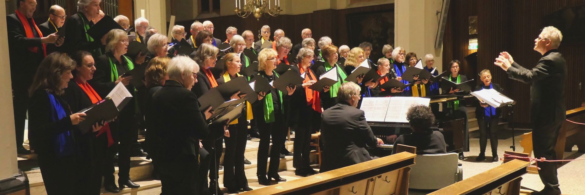 Een koor treedt op in een kerk onder leiding van een dirigent. De zangers houden bladmuziek vast.