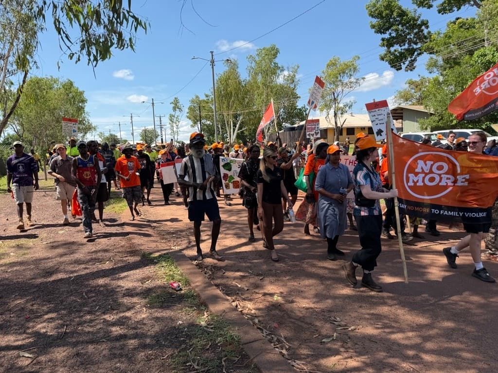 People marching down a dirt road, holding signs and a