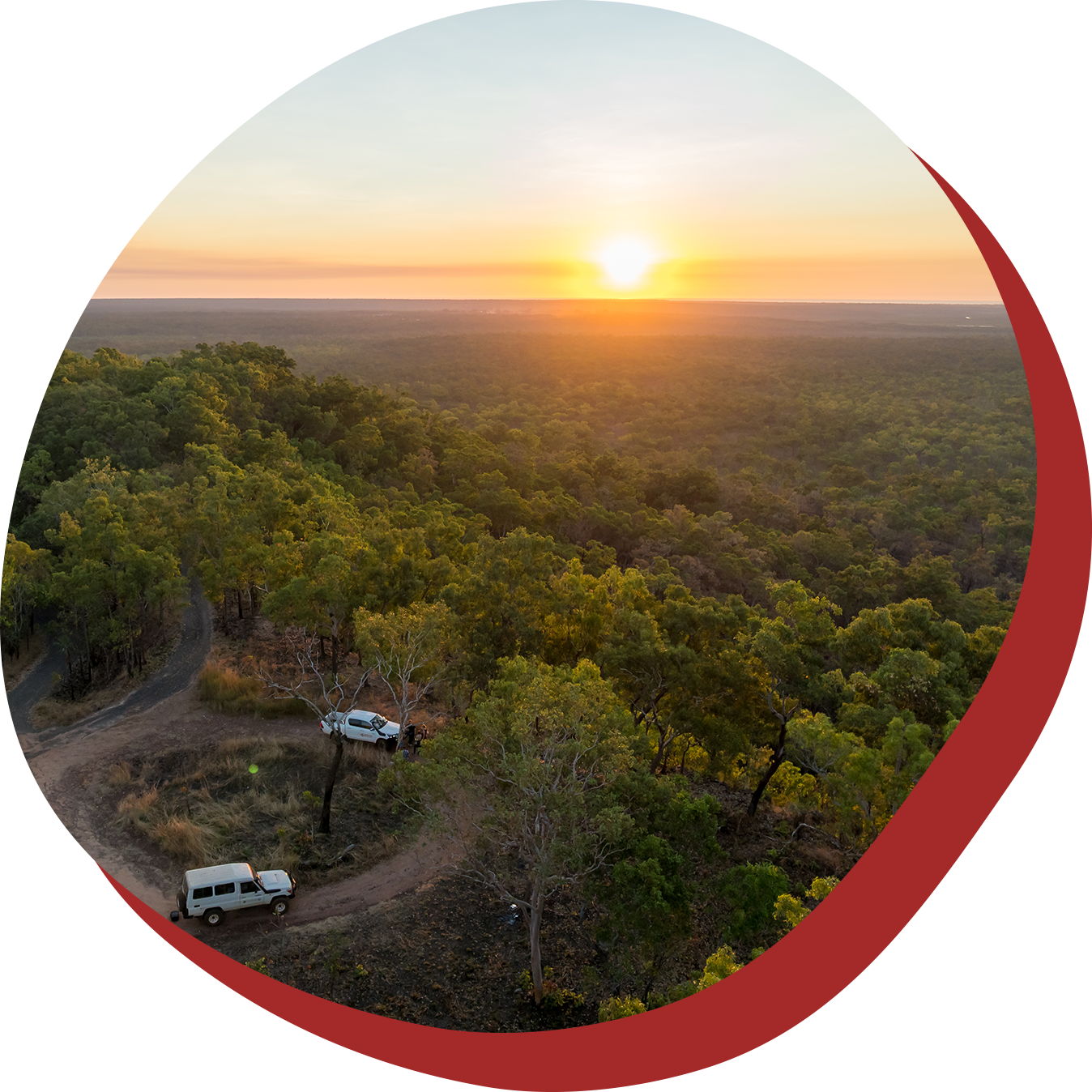 Two off-road vehicles on a dirt road in a forest at sunset, golden sky.