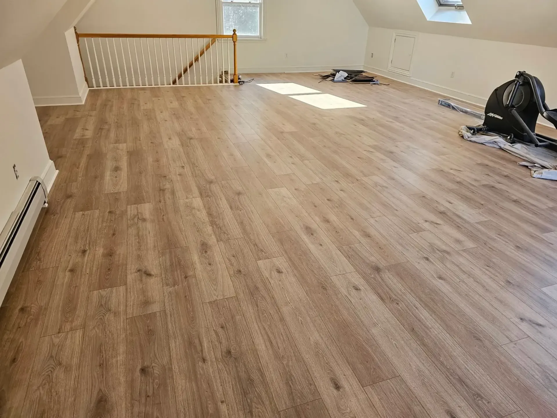 Bright room with wood-look flooring, sloped ceiling with small window, and a staircase with a white railing.